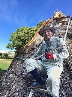 兵庫県立考古博物館 事業部長　髙瀬　一嘉さん <br/>建築中の竪穴住居の屋根に乗り、カヤを結束する竹製の針を手にしている